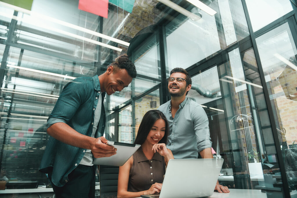 Happy to work together. Group of three young and positive employees using modern technologies and smiling while working in modern office